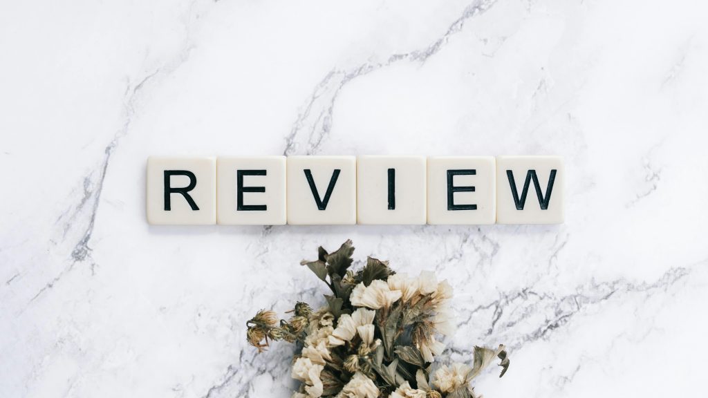 Scrabble tiles spelling 'REVIEW' on a marble surface with dried flowers.